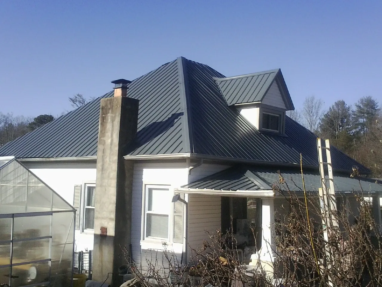Dark blue standing seam metal roof on a white farmhouse with dormer — Slate & Tile Roof Repair by Roofing Brothers in Amissville