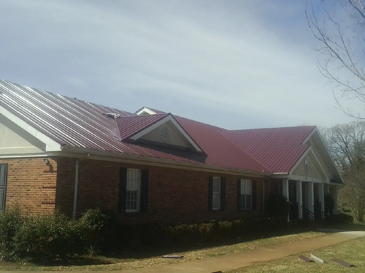 Red metal roof with gabled entries on a long brick building, from a Hail Damage Roof Repair job in Amissville
