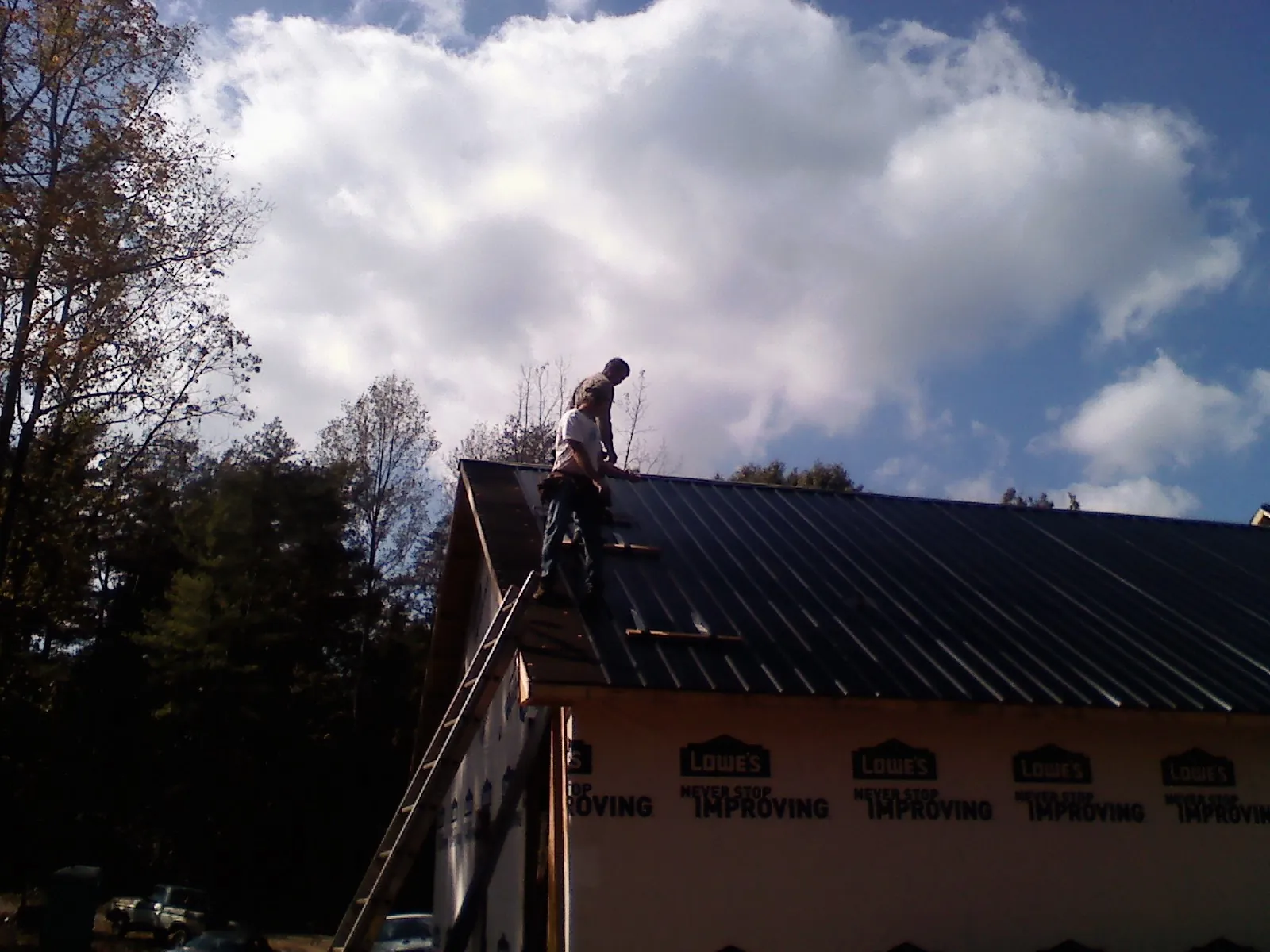 Roofer fastening dark metal panels high against a cloudy sky, from a Roof Inspection job in Amissville
