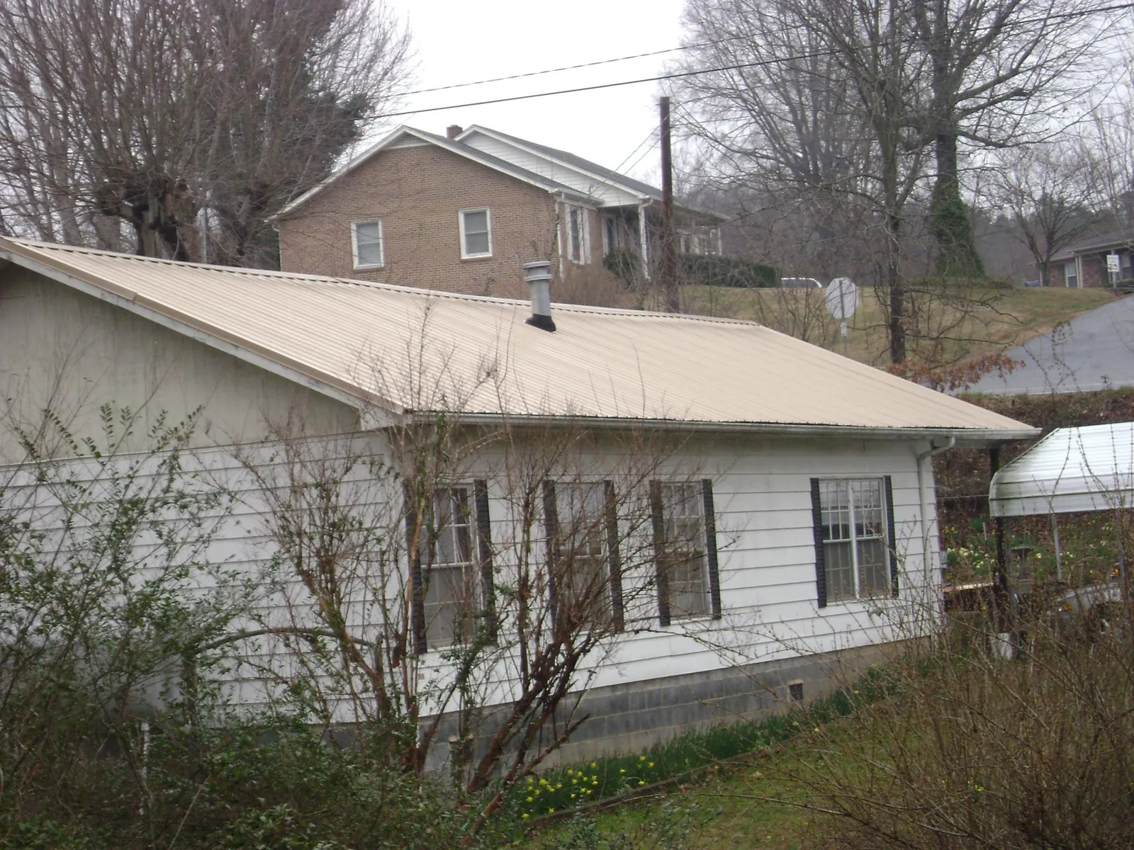 Tan metal roof on a white sided house set into a hillside — Commercial Roofing by Roofing Brothers in Amissville